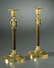 A fine pair of Empire gilt and patinated bronze candlesticks, each surmounted by an anthemion cast vase-shaped nozzle with gadrooned drip-pan above a tapering columnar stem headed by three Classical female heads 