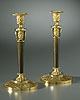 A fine pair of Empire gilt and patinated bronze candlesticks, each surmounted by an anthemion cast vase-shaped nozzle with gadrooned drip-pan above a tapering columnar stem headed by three Classical female heads